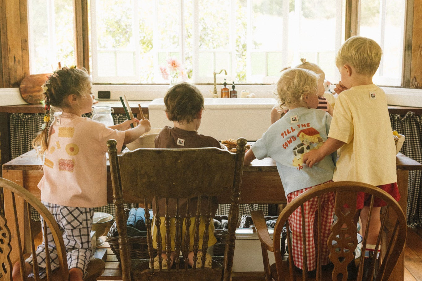 Children sitting at a wooden table in a room with large windows and green pendant lights.
